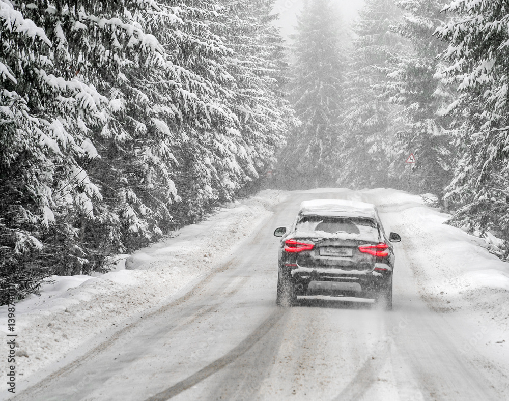 Beautiful winter scene with icy slick road driving car . Alpine road covered with water and ice and snowy trees all around