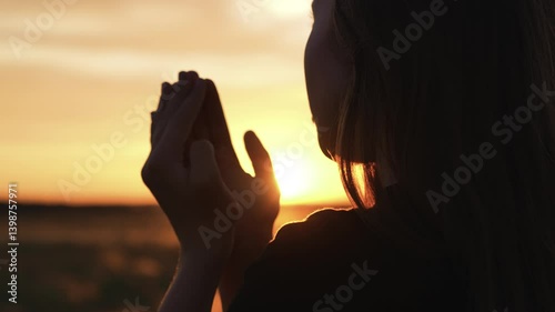 Woman praying with folded hands at sunset silhouette. Religious pious orthodox christian spiritual believing faithful girl at morning dawn sunrise reading prayer bible turning to god jesus christ.