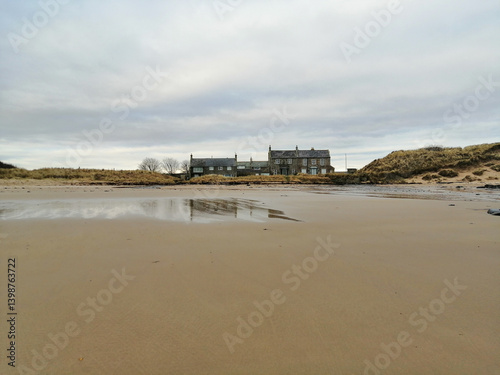 A beautiful beachfront scene featuring a building on the coast, with wet sand and a serene, cloudy sky.