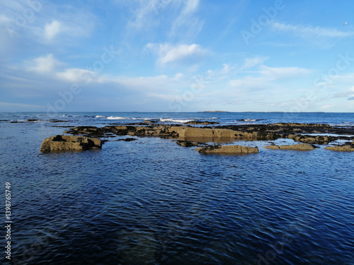 The ocean's embrace on a bright day, with rocks and water meeting the bright blue sky.