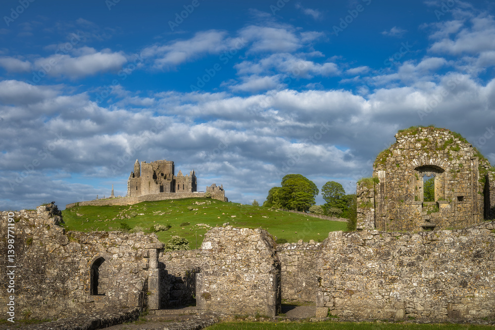 Ancient ruins of Rock of Cashel and Hore Abbey perched on a scenic hill, enveloped by lush greenery and soft clouds, providing a captivating glimpse into a rich history, Tipperary, Ireland