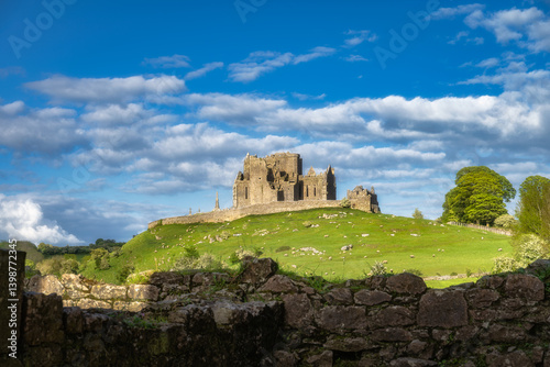 Explore serene and picturesque landscape that features magnificent historic ruins of Rock of Cashel and Hore Abbey perched atop a lush green hill all set against a vibrant blue sky, Tipperary, Ireland