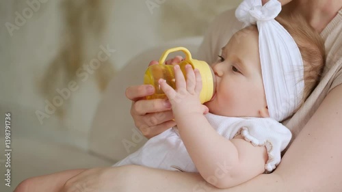 a mother feeds a baby from a bottle, a mother gives a small child water from a bottle while holding him in her arms at home