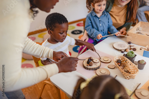 Diverse group of preschool children engage in a nature-based learning activity with two teachers, using wood and natural objects to explore creativity and tactile skills in the classroom.