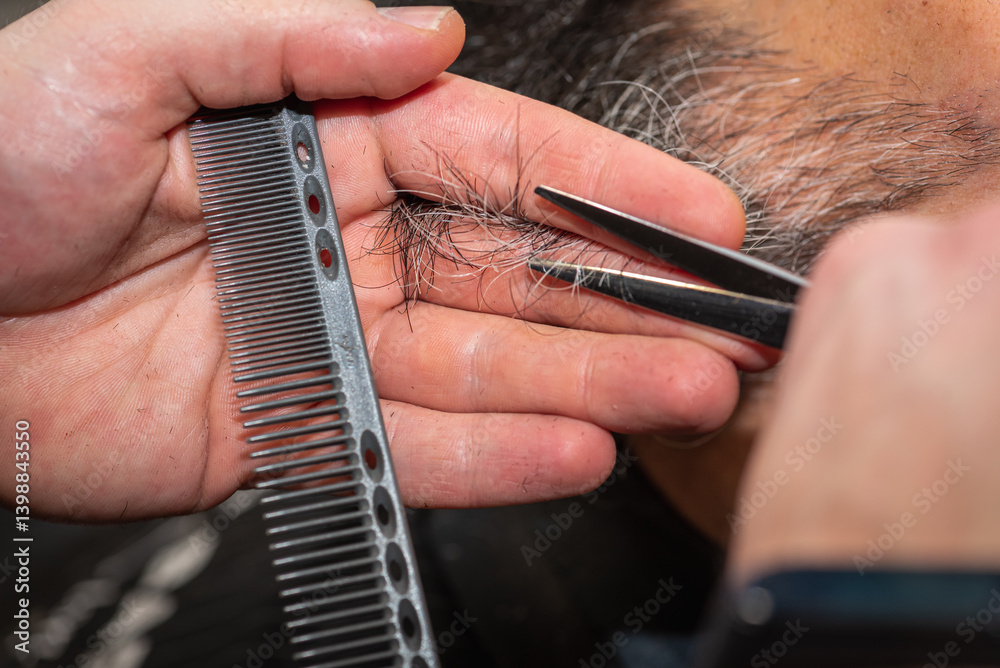 Close-up of a barber trimming a beard with electric clippers in a modern barbershop. Professional men's grooming and beard care service, selective focus