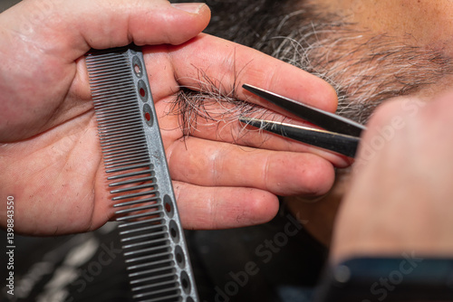 Close-up of a barber trimming a beard with electric clippers in a modern barbershop. Professional men's grooming and beard care service, selective focus