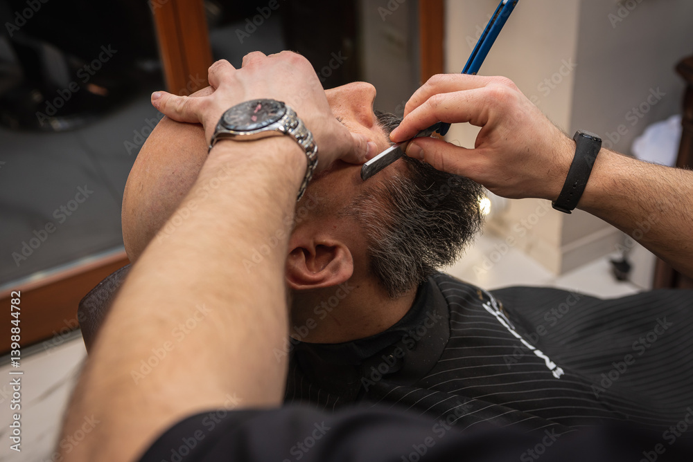 Close-up of a barber trimming a beard with electric clippers in a modern barbershop. Professional men's grooming and beard care service, selective focus