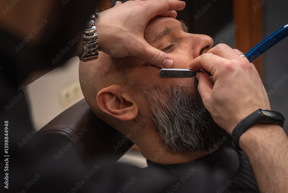Close-up of a barber trimming a beard with electric clippers in a modern barbershop. Professional men's grooming and beard care service, selective focus