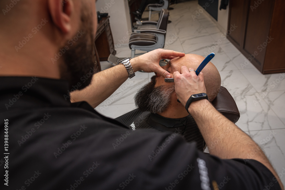 Close-up of a barber trimming a beard with electric clippers in a modern barbershop. Professional men's grooming and beard care, selective focus