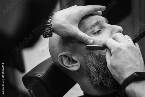 Obraz na płótnie Black and white classic vintage photo, close-up, barber trimming beard with electric clipper, hair scissors in modern barbershop. Professional men's grooming and beard care services, selective focus w salonie