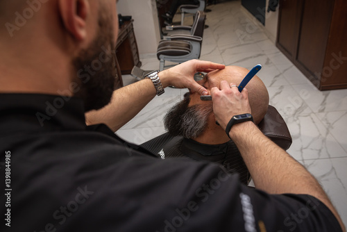Close-up of a barber trimming a beard with electric clippers in a modern barbershop. Professional men's grooming and beard care, selective focus