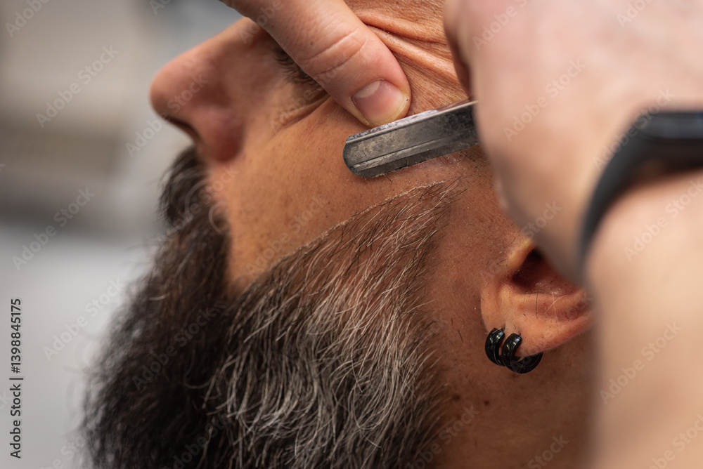 Close-up of a barber trimming a beard with electric clippers in a modern barbershop. Professional men's grooming and beard care service, selective focus