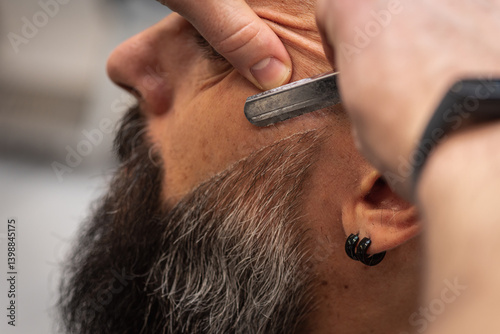 Obraz na płótnie Close-up of a barber trimming a beard with electric clippers in a modern barbershop. Professional men's grooming and beard care service, selective focus w salonie