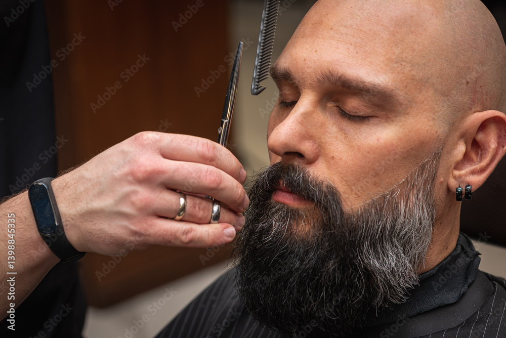Close-up of a barber trimming a beard with electric clippers in a modern barbershop. Professional men's grooming and beard care service, selective focus