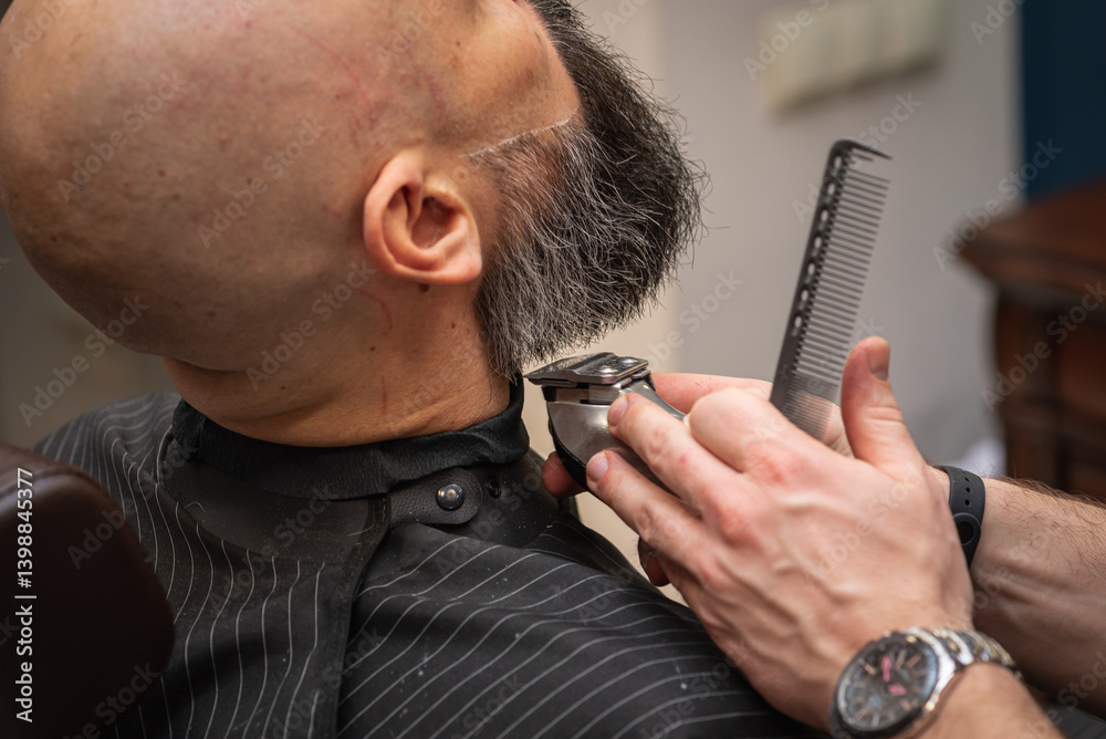 Close-up of a barber trimming a beard with electric clippers in a modern barbershop. Professional men's grooming and beard care service, selective focus