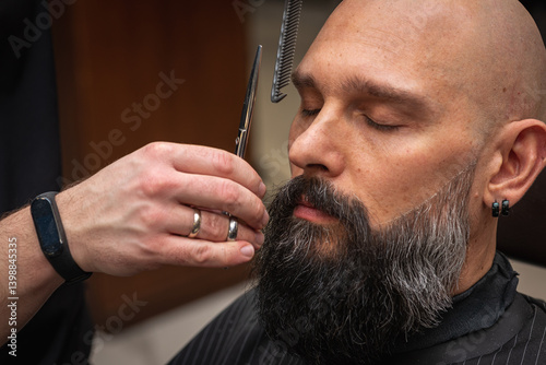 Close-up of a barber trimming a beard with electric clippers in a modern barbershop. Professional men's grooming and beard care service, selective focus