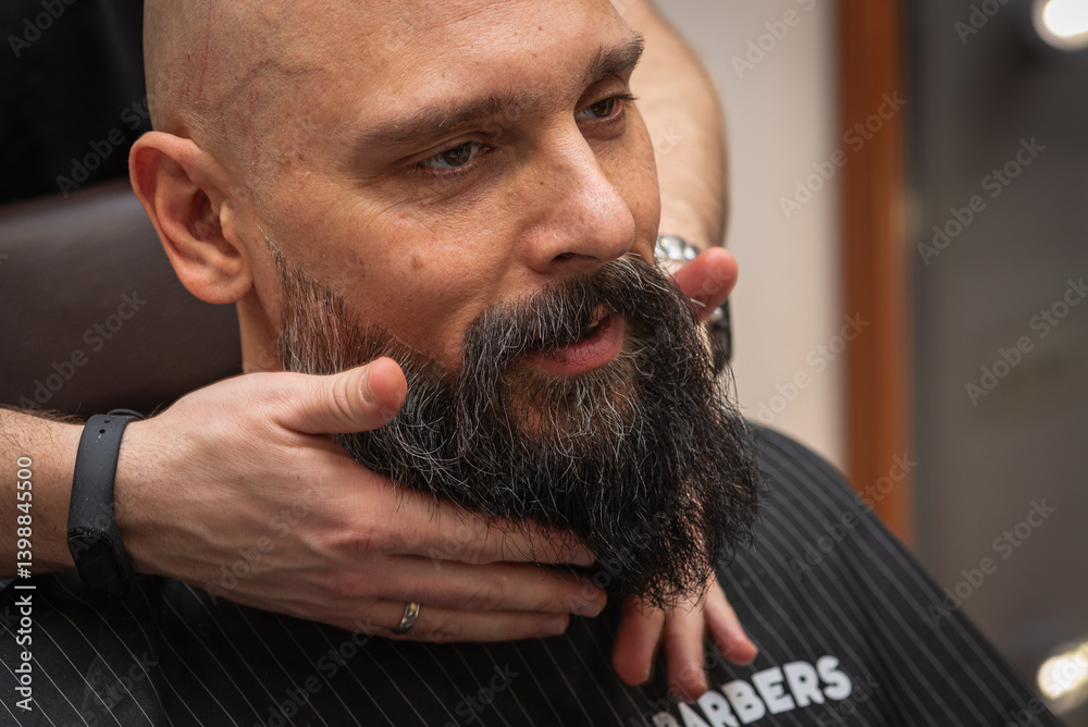Bearded man at barbershop getting beard groomed and shaped by barber. Close-up of grooming process, professional beard care, stylish male beauty routine