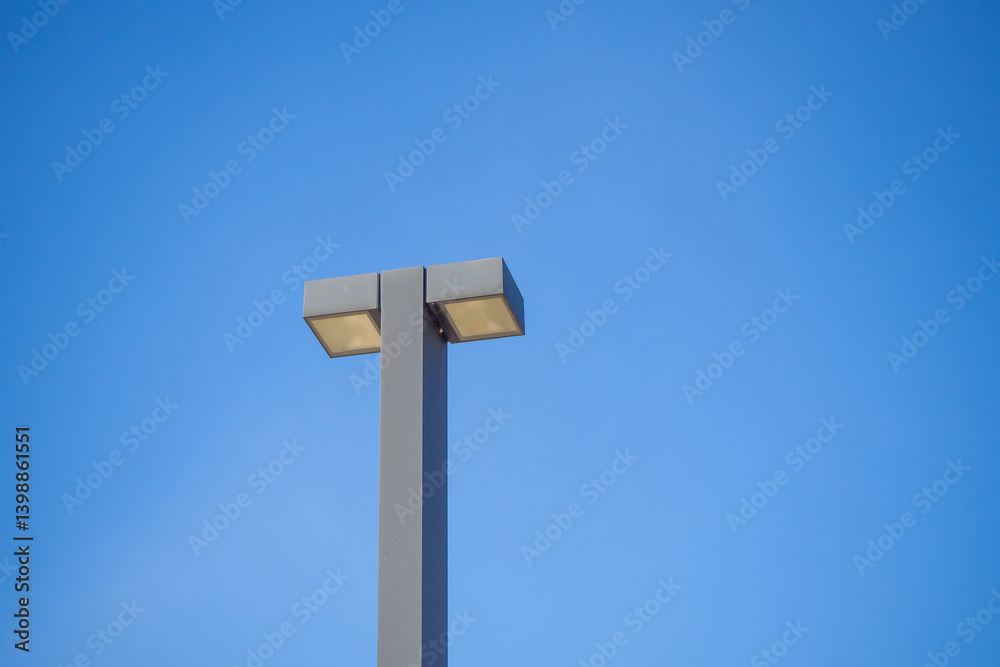 Tall twin-head streetlight against blue sky. Used in road and parking lot illumination..Symmetrical lamp design for efficient distribution of light in open space Tall twin-head streetlight against blue sky. Used in road and parking lot illumination..Symmetrical lamp design for efficient distribution of light in open space