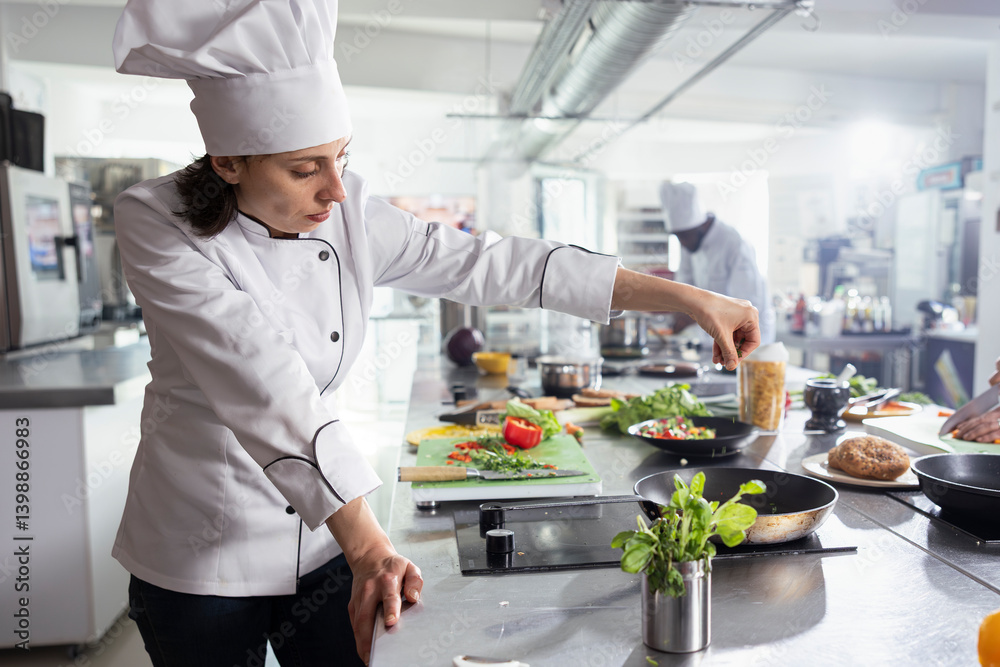 In a modern kitchen, woman head chef adding herbs to complete a gourmet dish, balancing flavors with rosemary and other greenery. Kitchen counter stacked with vegetables and food prep. In a modern kitchen, woman head chef adding herbs to complete a gourmet dish, balancing flavors with rosemary and other greenery. Kitchen counter stacked with vegetables and food prep.