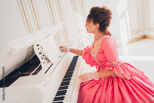 Elegant woman in pink gown playing piano in luxurious historical interior