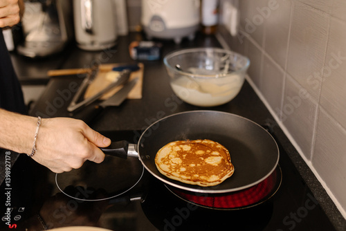 A close-up shot of a man flipping a pancake on a frying pan, soft focus.