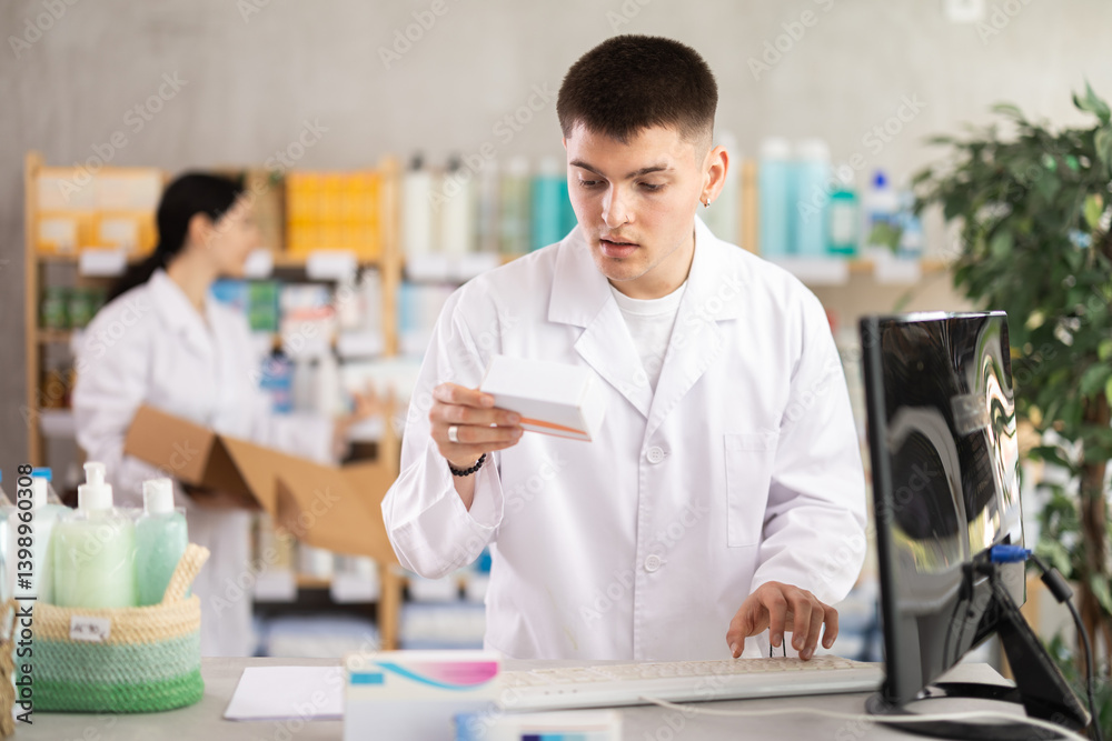 Near counter with computer is pharmacists workplace. Guy employee participates in online testing and learning, reads incoming emails. Electronic database of drugs. Colleague work in background Near counter with computer is pharmacists workplace. Guy employee participates in online testing and learning, reads incoming emails. Electronic database of drugs. Colleague work in background
