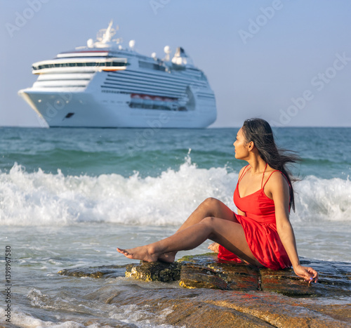 Obraz na płótnie A woman in a red dress sits on a rock in the sea and watches a large cruise ship sailing along the coast w salonie