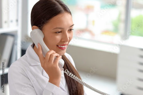 Young female medical receptionist talking on phone in hospital