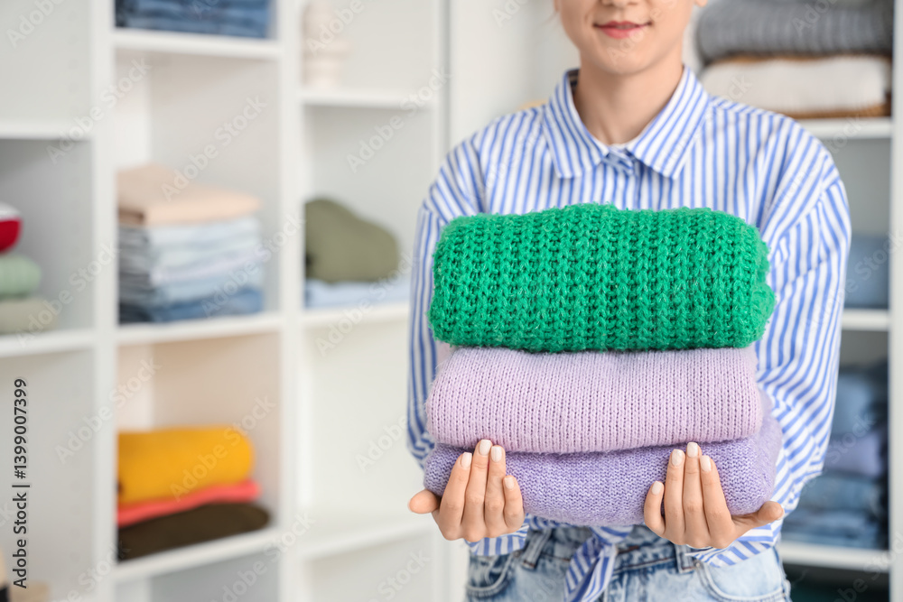 Young woman with stack of warm sweaters in dressing room. Closeup