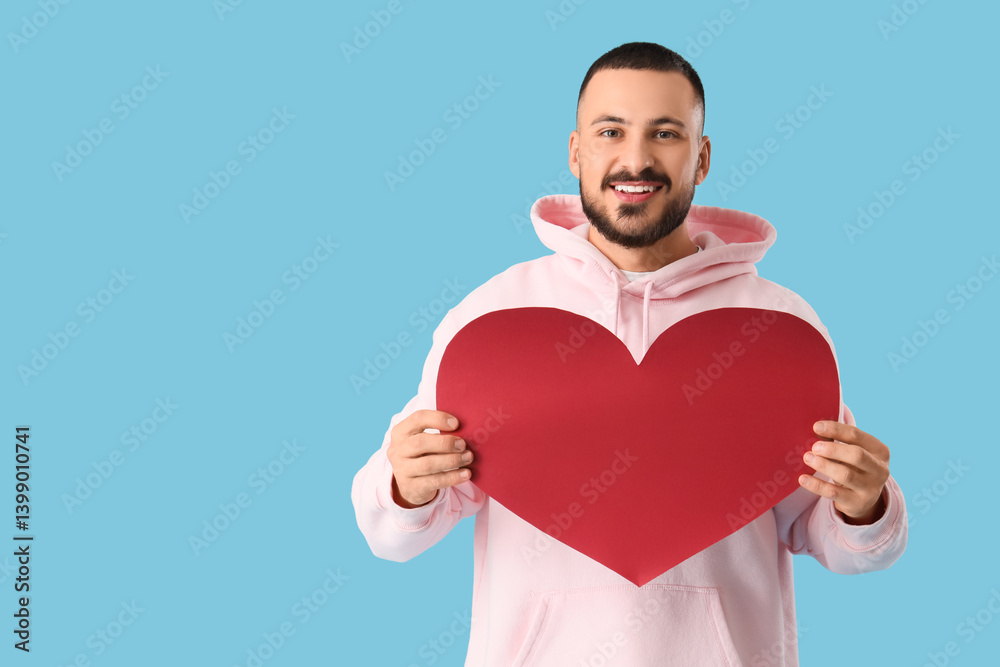 Handsome young man with paper heart on blue background Handsome young man with paper heart on blue background