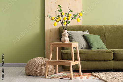 Interior of living room with green sofa, tree branches and lemons in vase