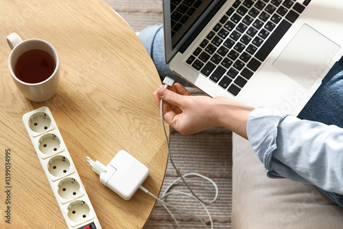 Young woman getting out charger from laptop at home, top view. National Day of Unplugging