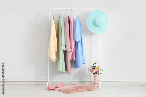 Rack with stylish female clothes, hat, shoes and flowers near light wall