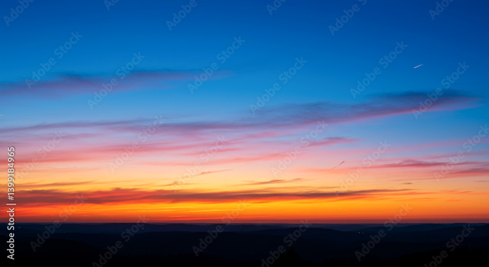 Fototapeta premium A vibrant sunset paints the sky with fiery colors above a dark, silhouetted mountain range. The scene captures the tranquility and beauty of nature at dusk.