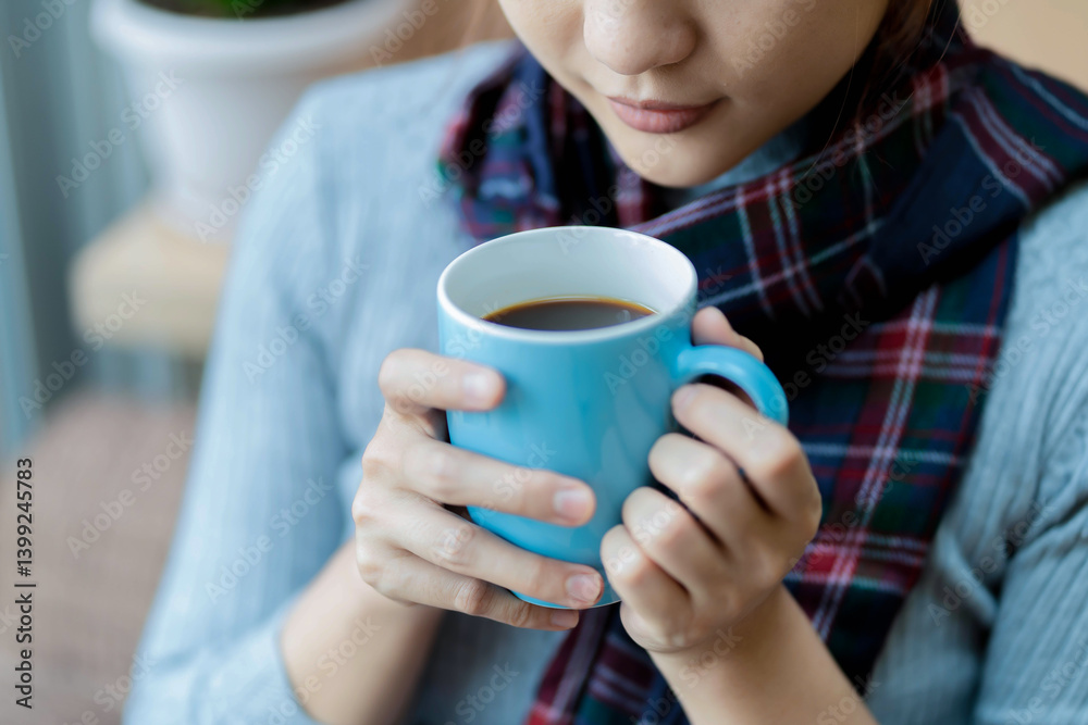 Close-up of woman gently holding a blue coffee mug while wearing a cozy plaid scarf, enjoying a moment of calm and warmth in a relaxed indoor environment Close-up of woman gently holding a blue coffee mug while wearing a cozy plaid scarf, enjoying a moment of calm and warmth in a relaxed indoor environment
