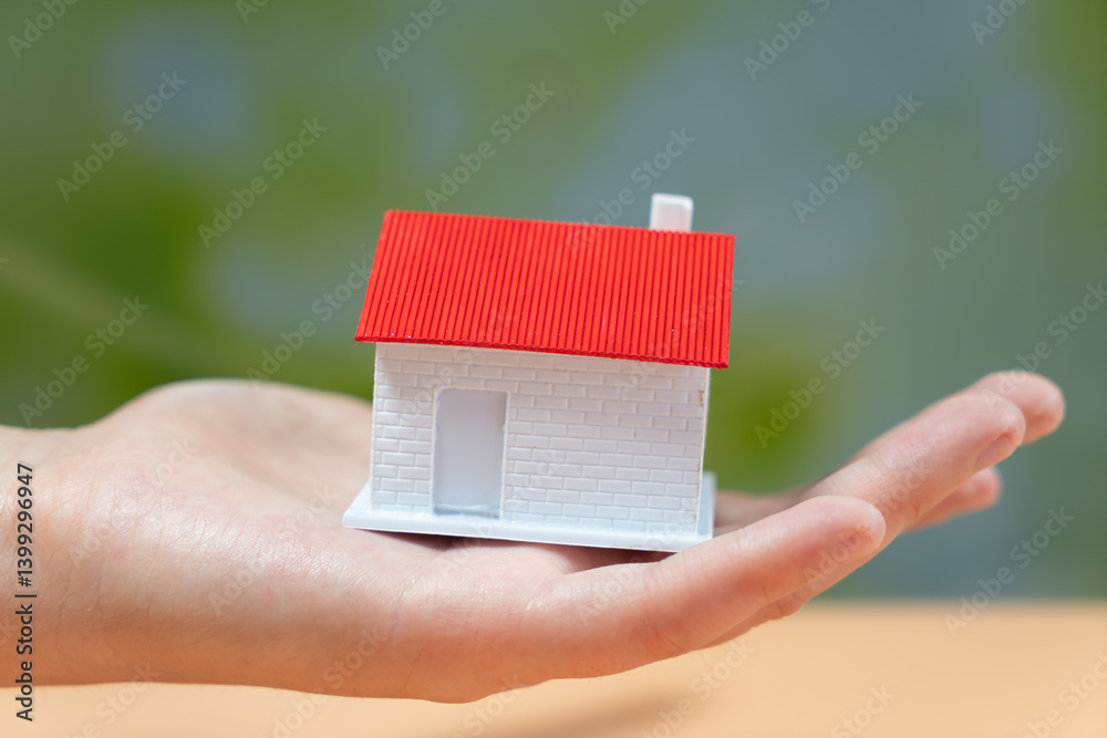 A Hand Holding a Model House Signifying Homeownership and Care