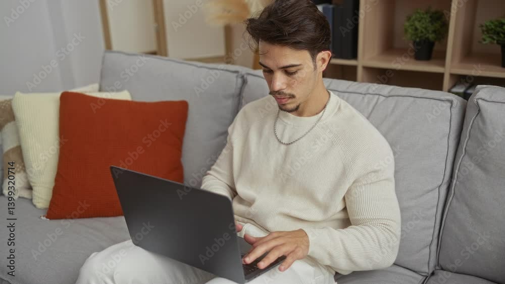 Young man using laptop on sofa in a cozy living room setting with soft cushions and plants in background surroundings, showcasing relaxed home environment and focus. Young man using laptop on sofa in a cozy living room setting with soft cushions and plants in background surroundings, showcasing relaxed home environment and focus.