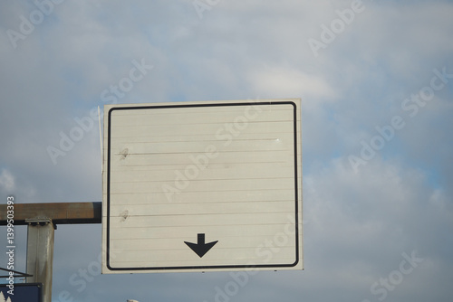 Fototapeta Naklejka Na Ścianę i Meble -  Blank traffic sign points downward amidst a cloudy sky