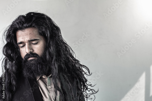 Fotografi A man with long, dark, wavy hair and a full beard is shown from the chest up