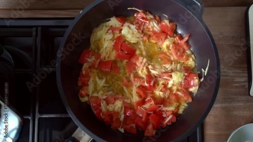 Zucchini and tomatoes are fried in a pan on the stove. Top view.