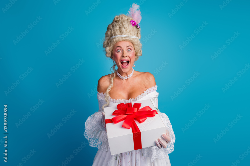Fototapeta premium Excited woman dressed as a baroque queen holding a gift boasting a vibrant red ribbon, set against a solid blue backdrop