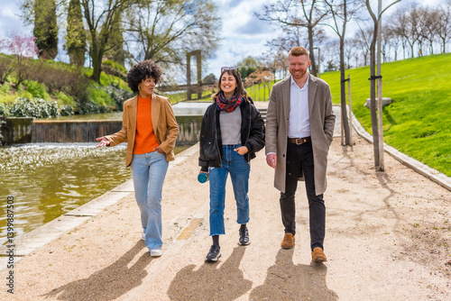 Obraz na płótnie Three colleagues walking and talking in a park near a pond w salonie
