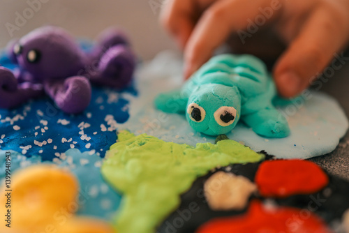 Colorful sea-themed scene made from modeling clay with a handmade turtle and octopus. A child’s hand plays with the turquoise turtle on a textured ocean base photo