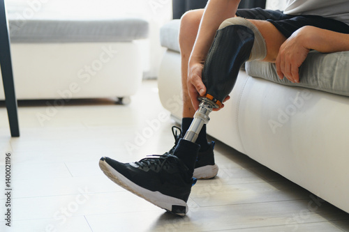 Man amputee with prosthetic leg disability on above knee transfemoral leg prosthesis wearing shoe sitting on sofa, close up. People with amputation disabilities everyday life concept