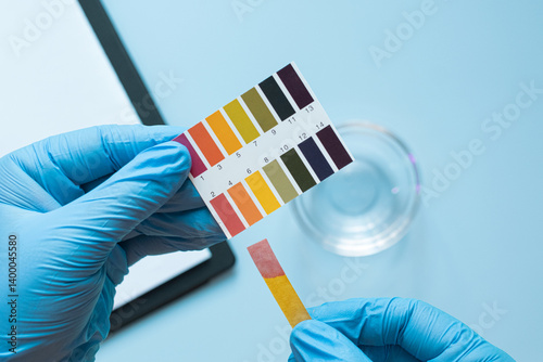 Gloved hands testing ph level with color chart and strips in laboratory setting. Acidic pH environment.