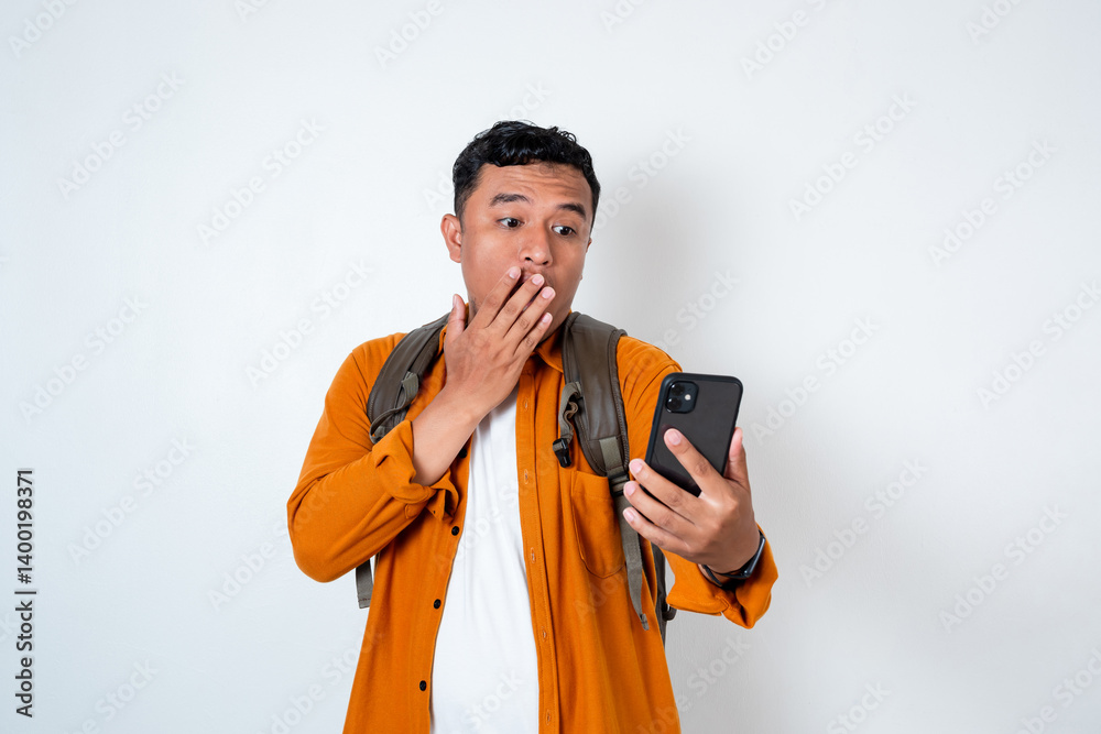 Image of handsome young Asian student holding cellphone and using backpack with shocked expression on isolated white background Image of handsome young Asian student holding cellphone and using backpack with shocked expression on isolated white background