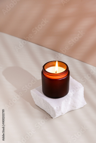 Soy wax burning candle in a dark glass jar on a beige background with shadows, minimalistic still life photo