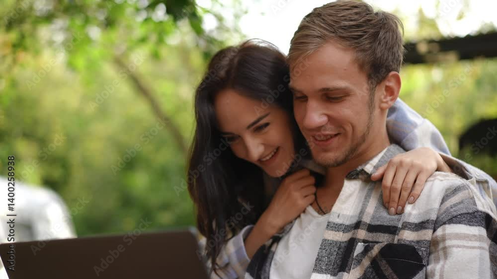 A truly happy couple shares a joyful and delightful moment together as they use a laptop in a serene outdoor setting A truly happy couple shares a joyful and delightful moment together as they use a laptop in a serene outdoor setting