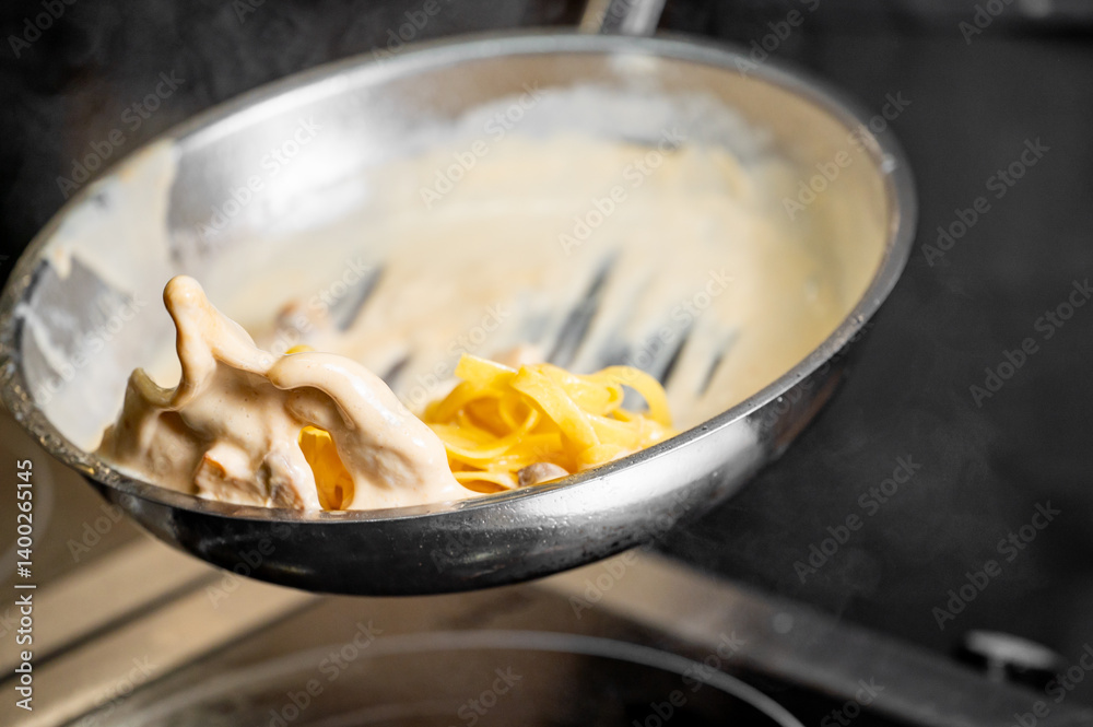 A close-up of creamy fettuccine being tossed in a stainless steel pan, showcasing rich sauce and steam, emphasizing the art of cooking in a modern kitchen.