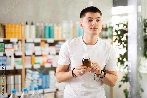Young man buyer selects expectorant syrup, reads composition, finds out information about use of drug. Medicines for treatment and prevention. photo